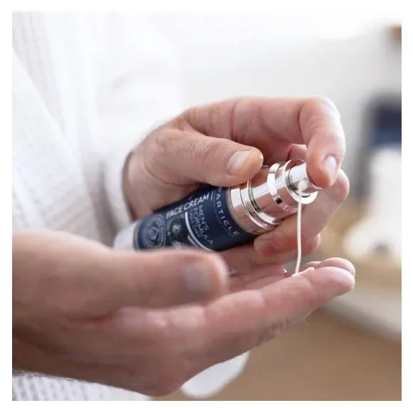 A close-up of a person's hands dispensing face cream from a dark blue and silver bottle onto their palm.